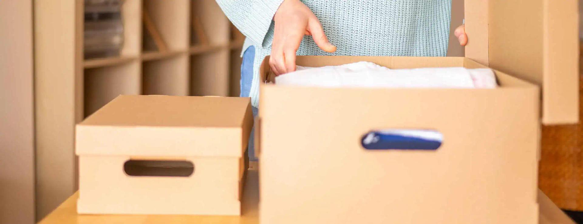Person carefully packing household items into boxes using moving tips.